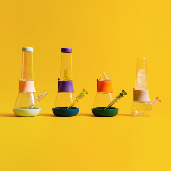 A row of custom bongs with colorful mix-and-match designs, displayed against a yellow background.